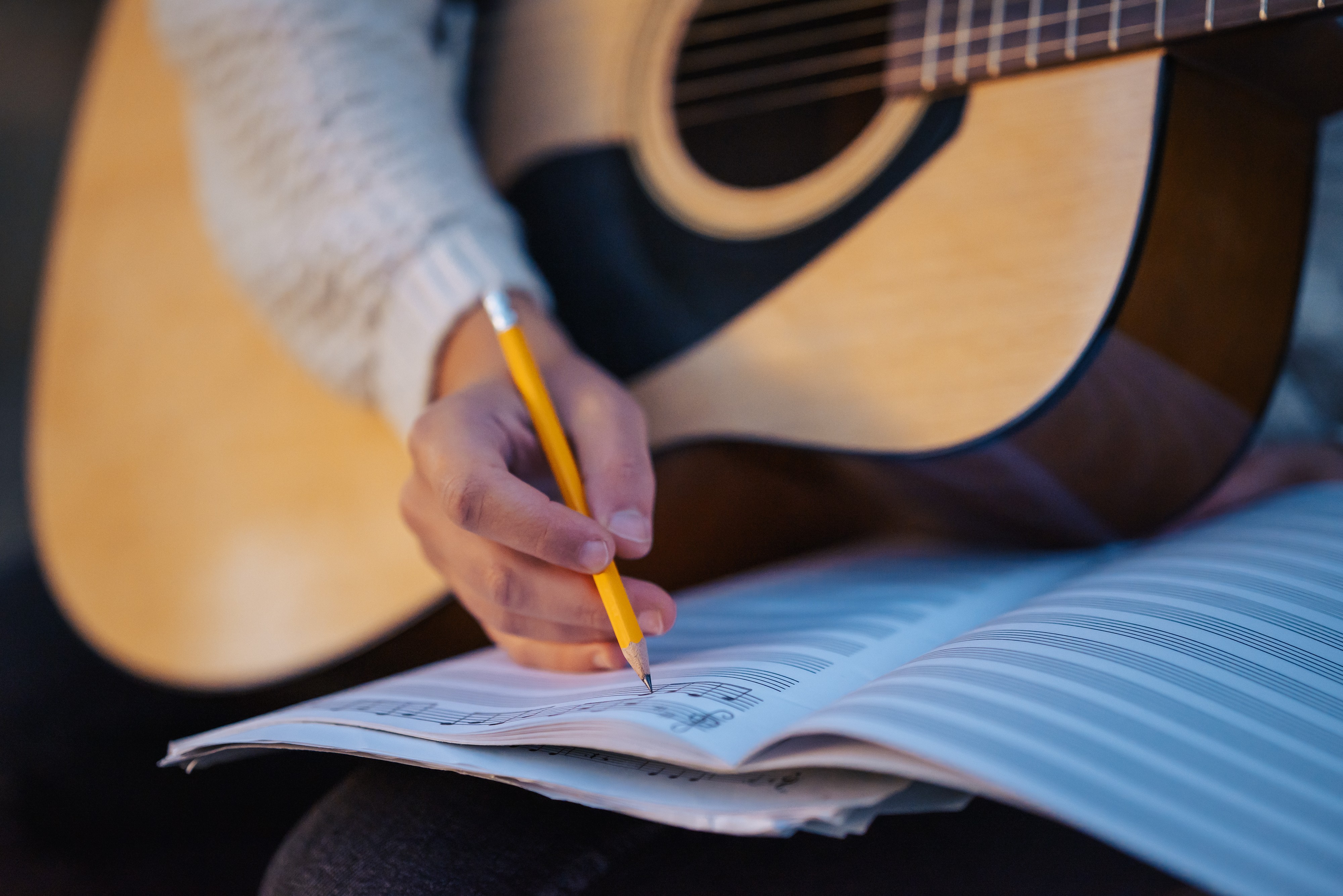womans-hand-writing-notes-her-notebook-while-playing-guitar-close-up